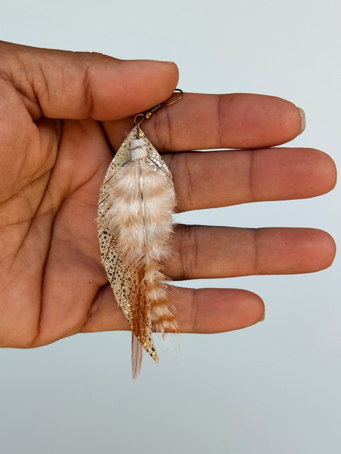 Single Golden Whisper Feather Earring held by hand to show its size