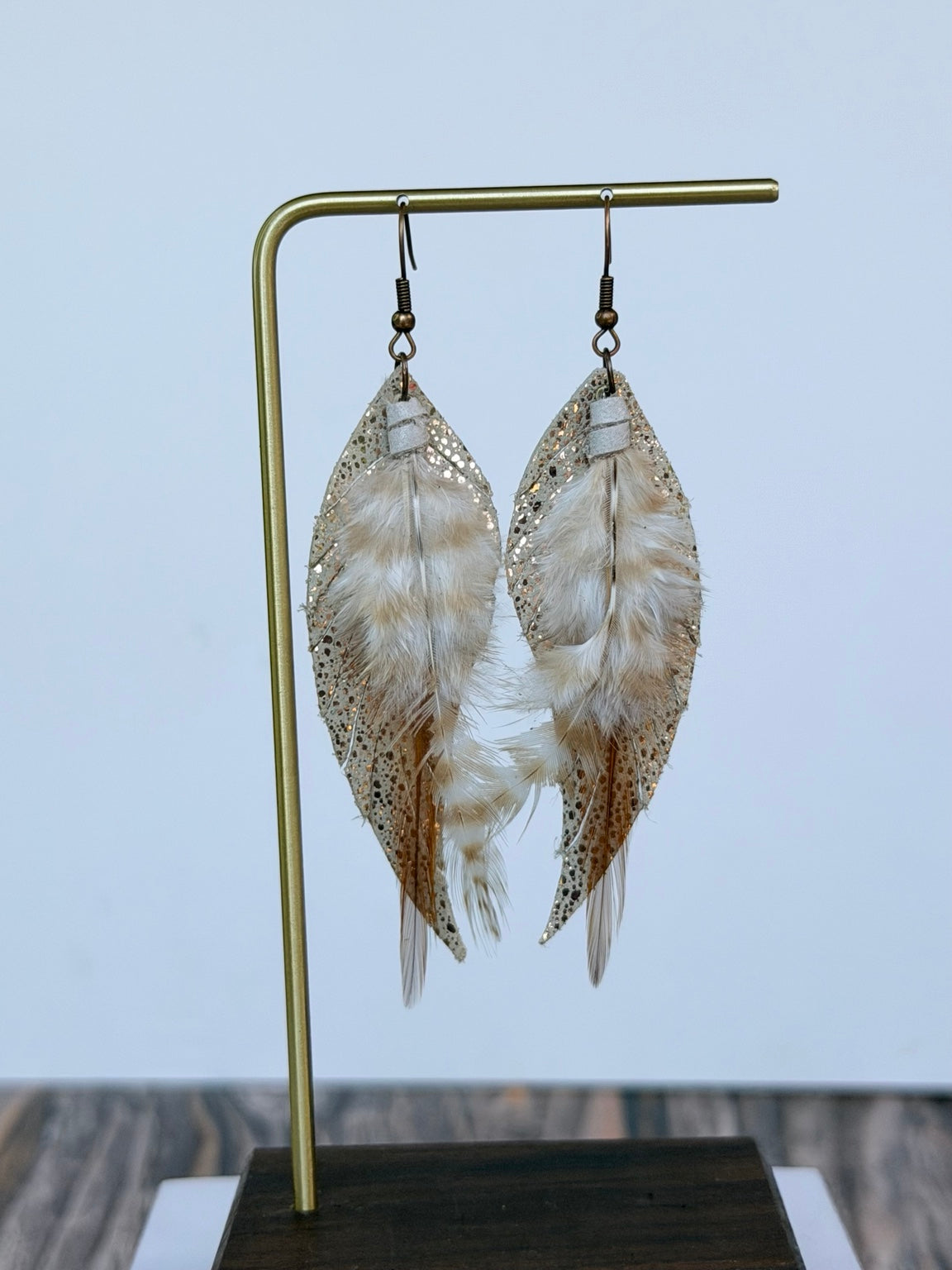 Golden Whisper Feather Earrings displayed on a gold jewelry stand