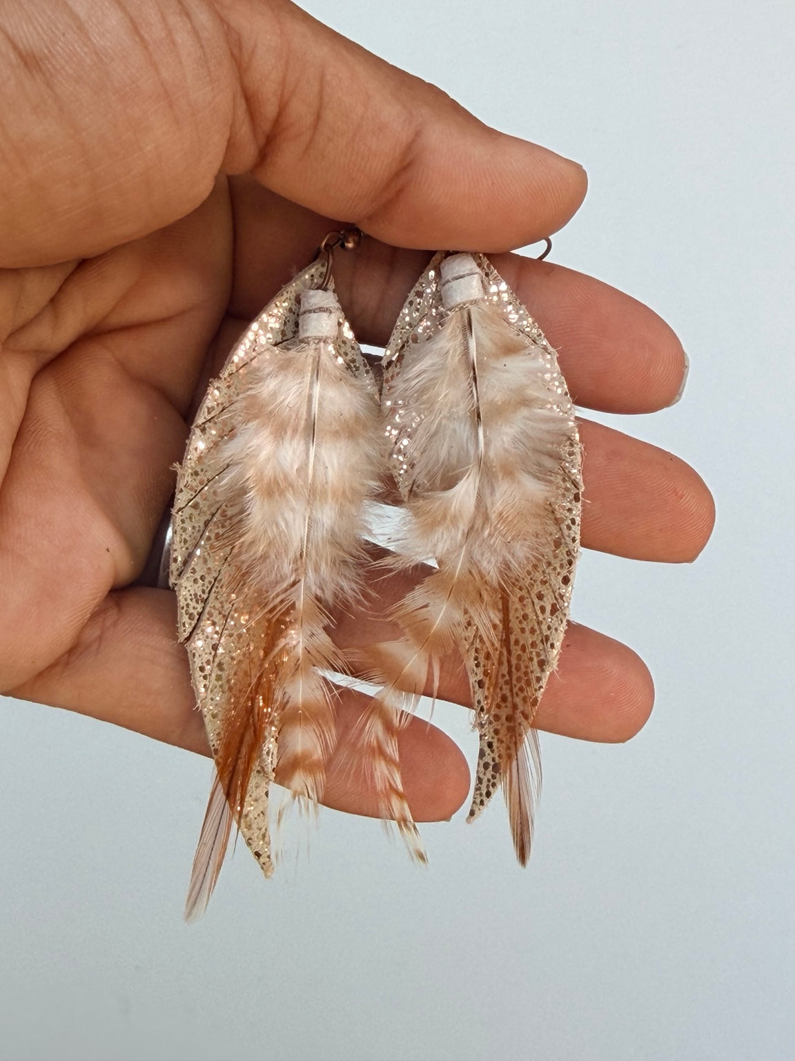 Golden Whisper Feather Earrings held by hand to show their layered detail