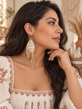 Latina model wearing Golden Whisper Feather Earrings with an embroidered ivory blouse