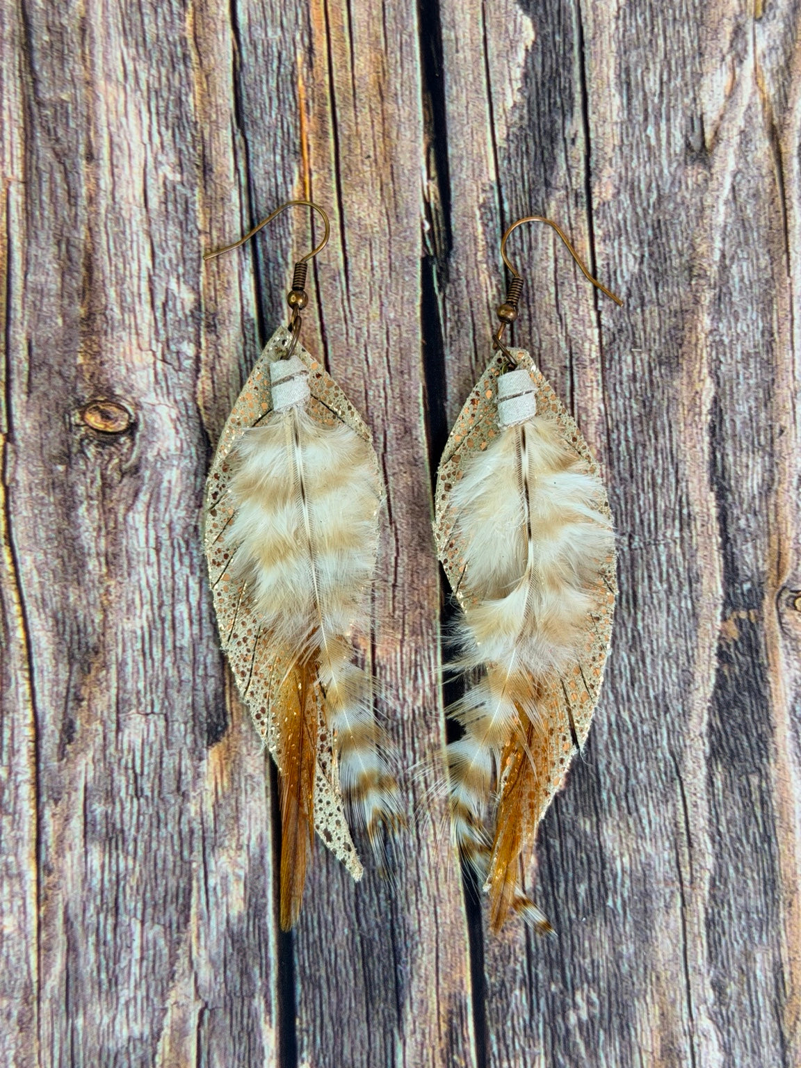 Pair of Golden Whisper Feather Earrings on a rustic wood background